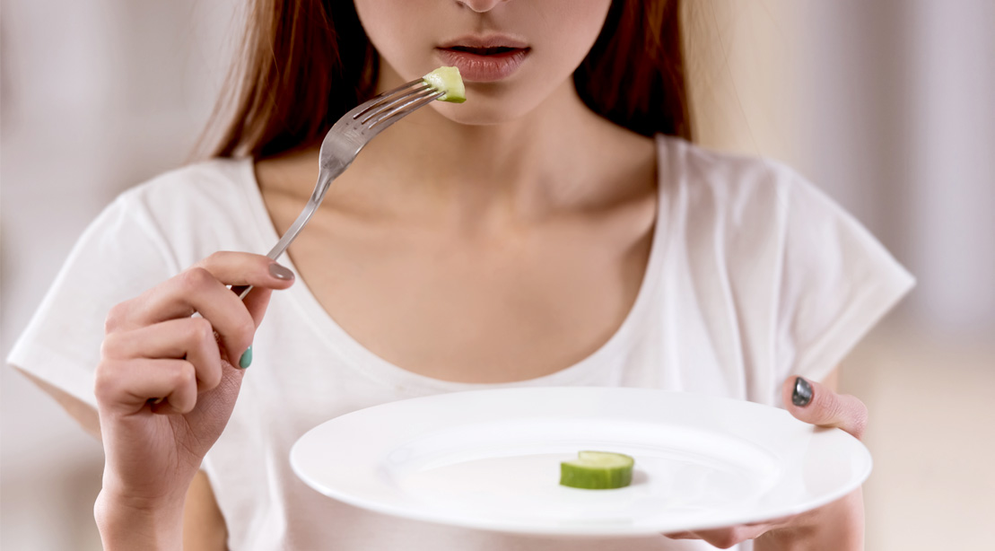 Young-Girl-using-a-fork-to-eat-a-small-slice-of-cucumber-on-a-plate