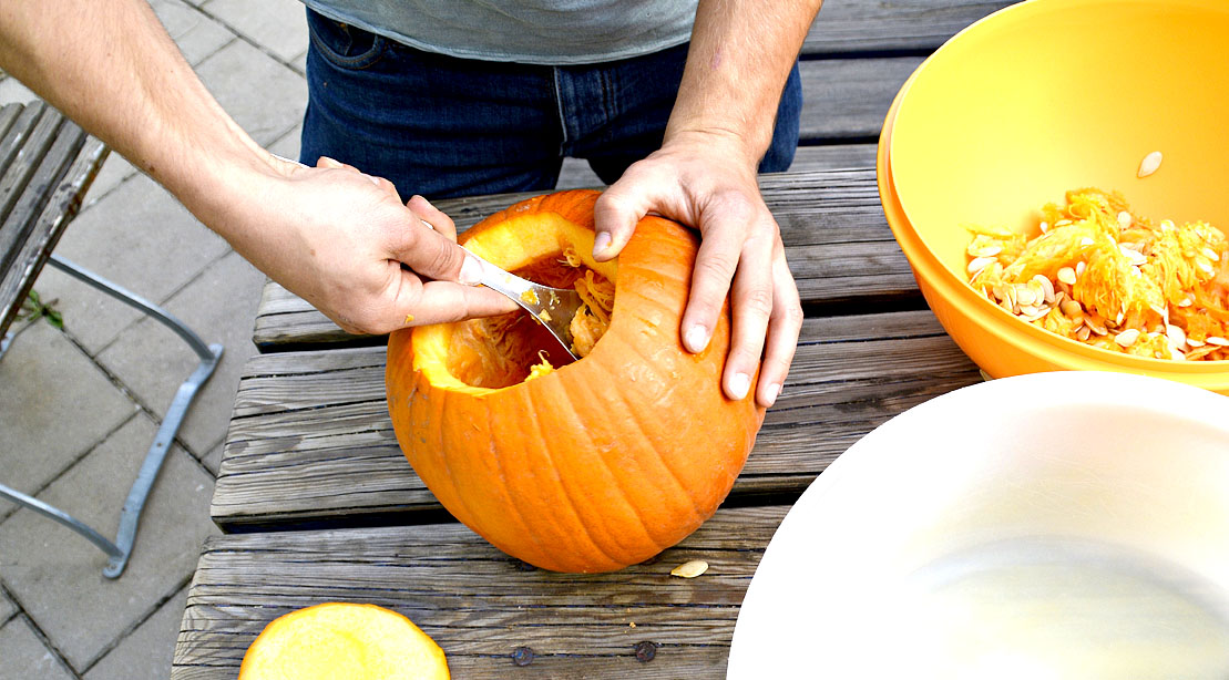 Man scooping out the flesh of a pumpkin and separating the pumpkin seeds