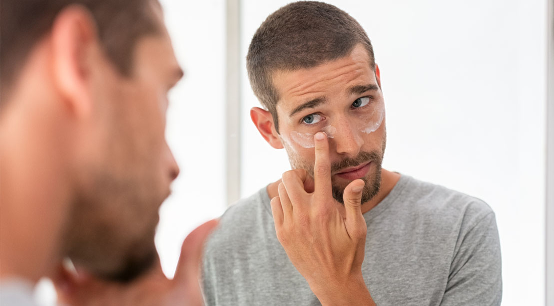 Man applying lotion to his skin and looking in the mirror