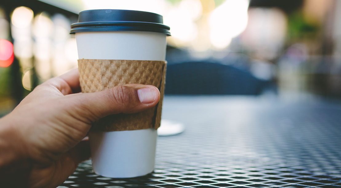 Man's hand holding a cup of coffee in a to-go cup