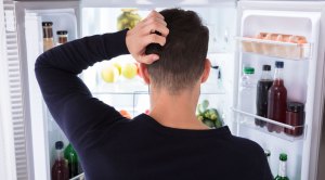 Confused Male Standing In Front Of His Fridge Looking At Which Foods Will Help Him Gain Weight Fast