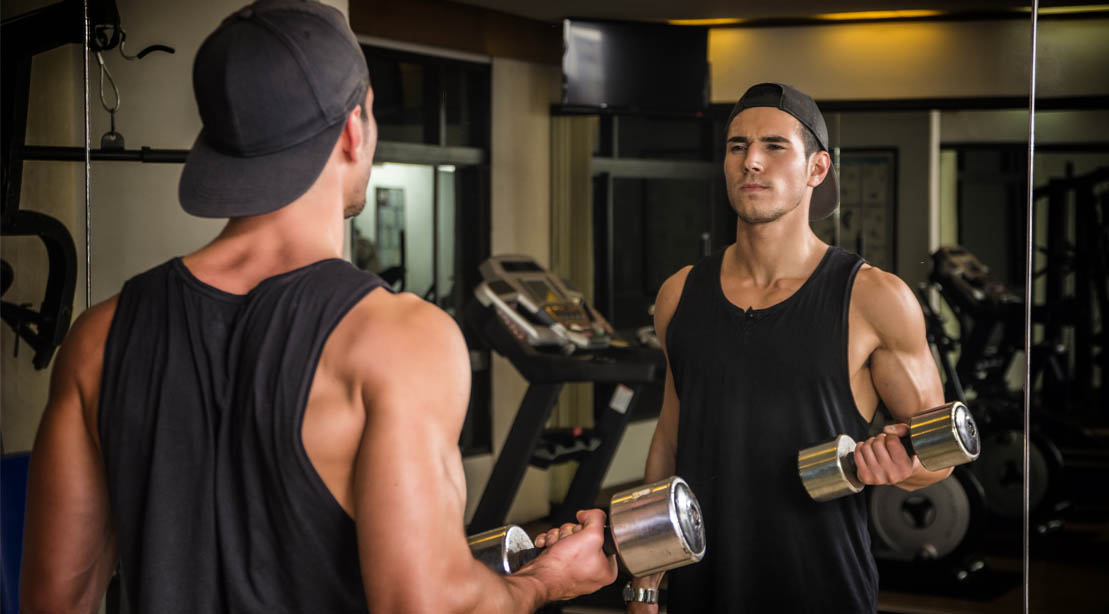 Young fit male doing upper arm workout with a bicep curl exercise in front of a mirror