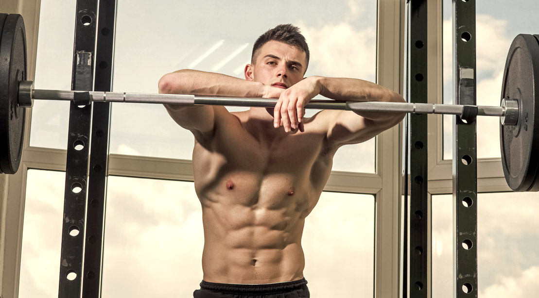 Young muscular fitness model standing in the barbell bench