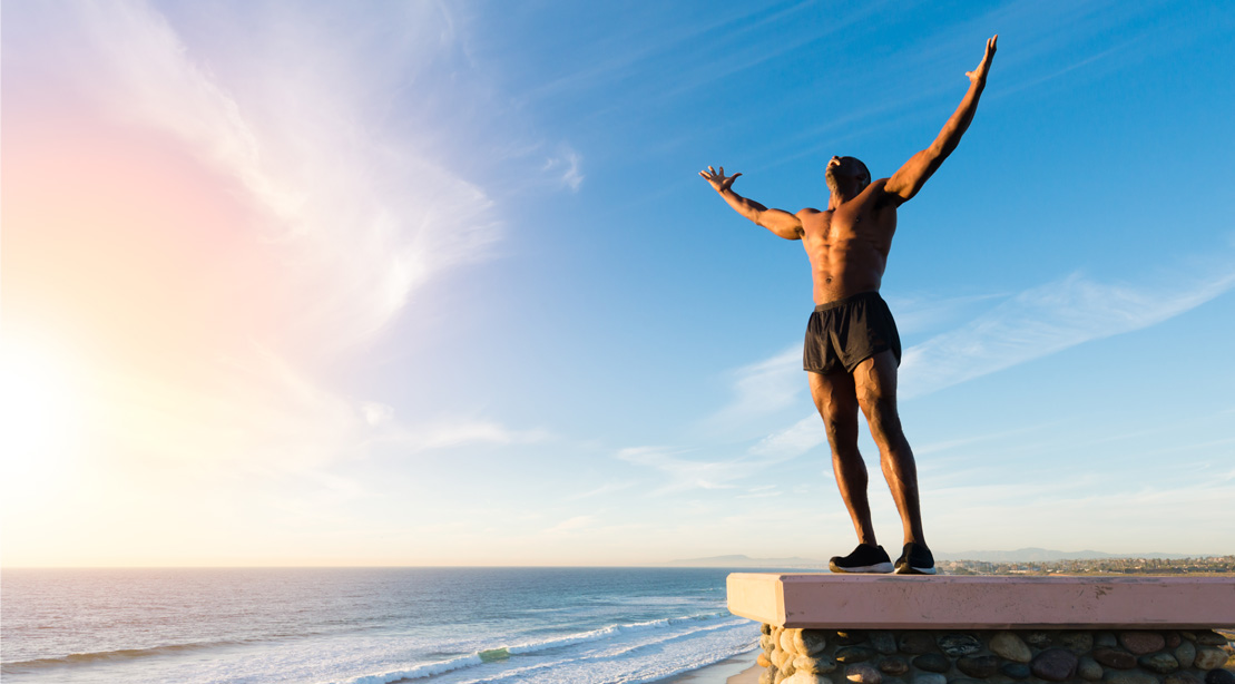 Man on a cliff with his arm stretched out in victory after a summer workout
