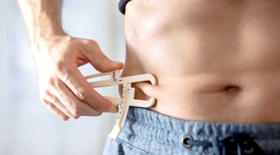 Fit man measuring his belly fat with calipers
