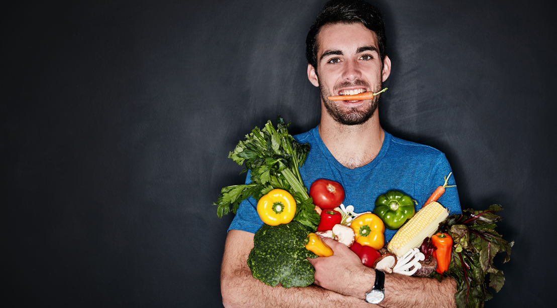 Man holding a carrot in his mouth while holding a bag of vegetable and produce for his volumetrics diet and shopping at his online grocery site