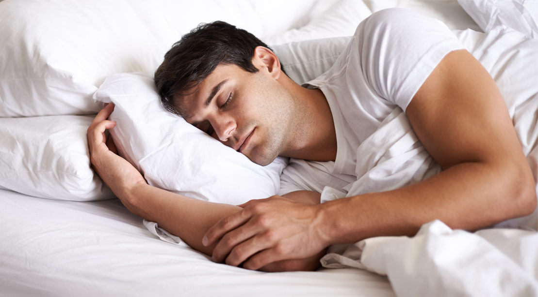 Muscular man sleeping deeply on a bed and pillow under his head