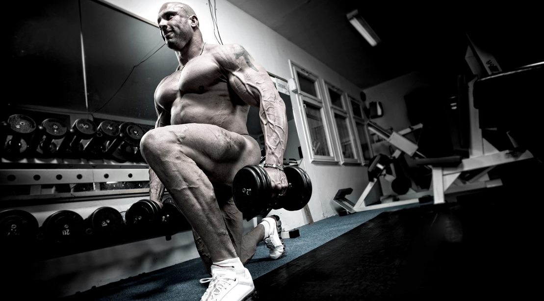 Bald bodybuilder doing dumbbell leg workouts with a dumbbell split squat exercise