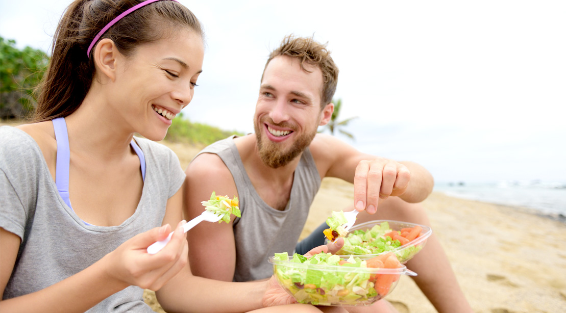Healthy conscious couple eating a salad on the beach