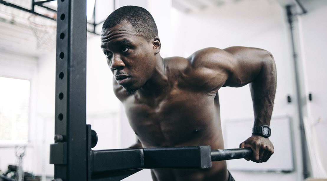 Muscular black man working out his arms and back by doing dip exercise and dip variations