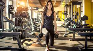 Woman performing a deficit reverse lunge at the gym while holding dumbbells