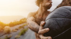 Fit muscular man performing lateral exercises using a medicine ball during sunrise on an empty road for his med ball training exercises