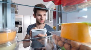 Young man with a note pad writing down a refrigerator food list