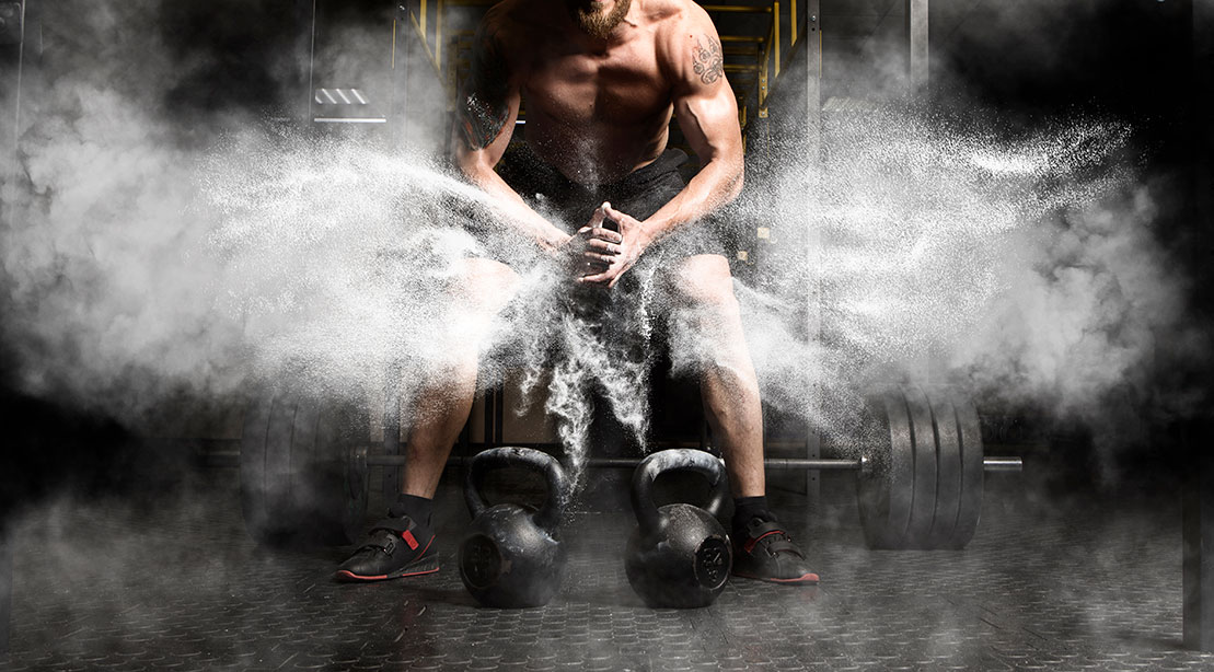 Fit male preparing for a kettlebell workouts and creating a cloud of chalk for extra grip