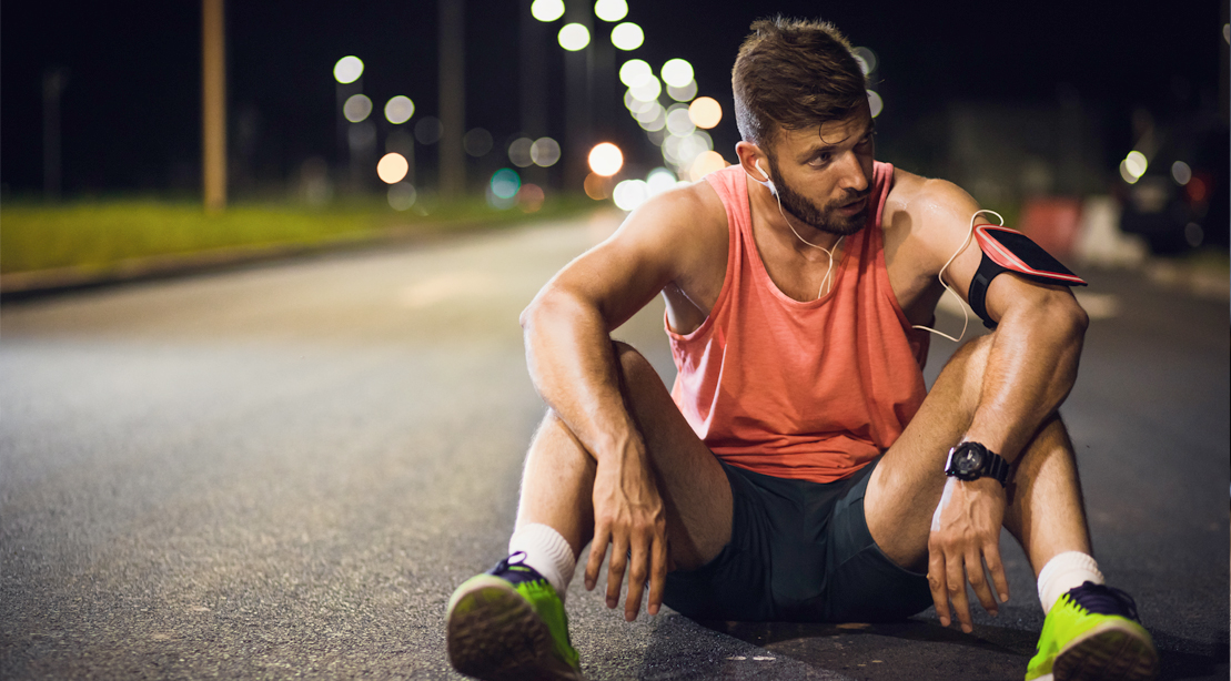 Male-Jogger-Resting-In-Middle-Of-Road-At-Night