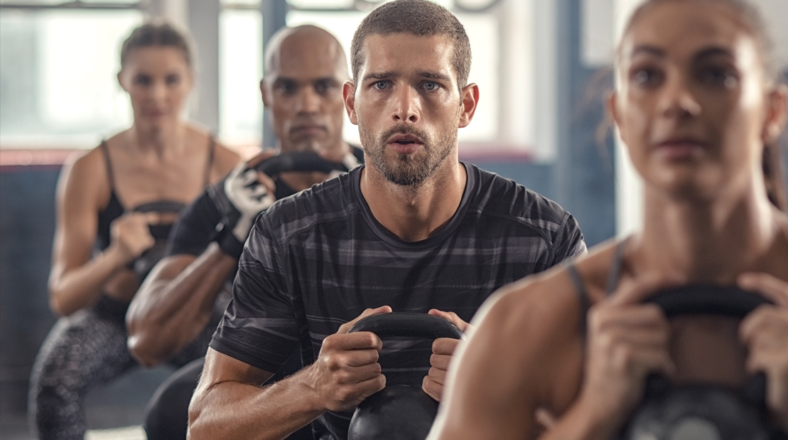 Sweaty-Confused-Man-In-Group-Fitness-Class-Performing-Kettlebell-Squat