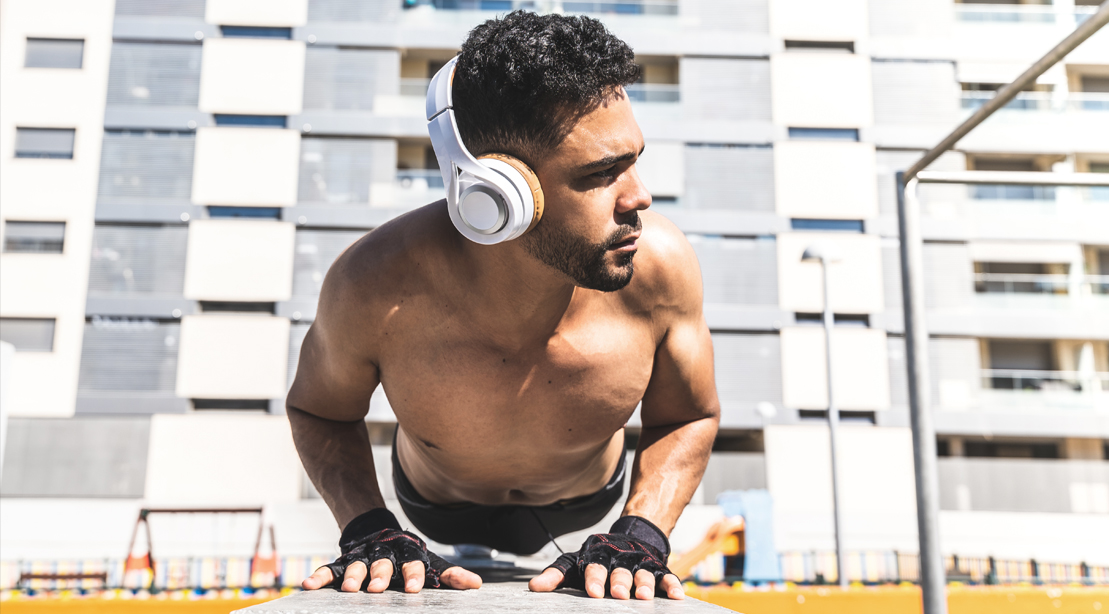 Fit male wearing headphones while doing pushup exercise in an apartment complex