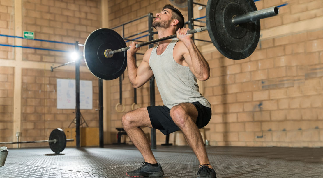 Skinny young man doing barbell squat exercise