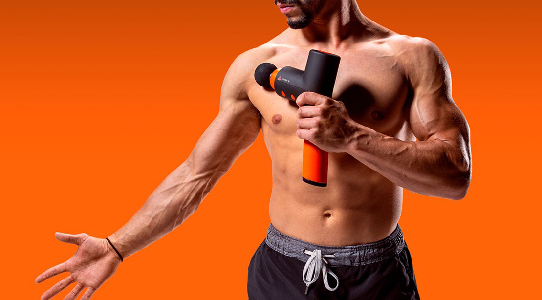 Fit lean muscular man using a jawku gun massager on his shoulder