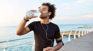 Black runner drinking a bottle of water as a good running tip and avoid dehydration