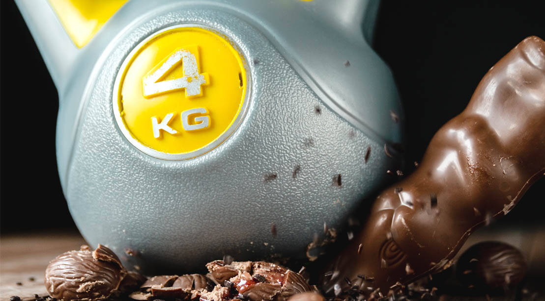 A 4 kilogram kettlebell weight cruching a chocolate candy bar and easter candies
