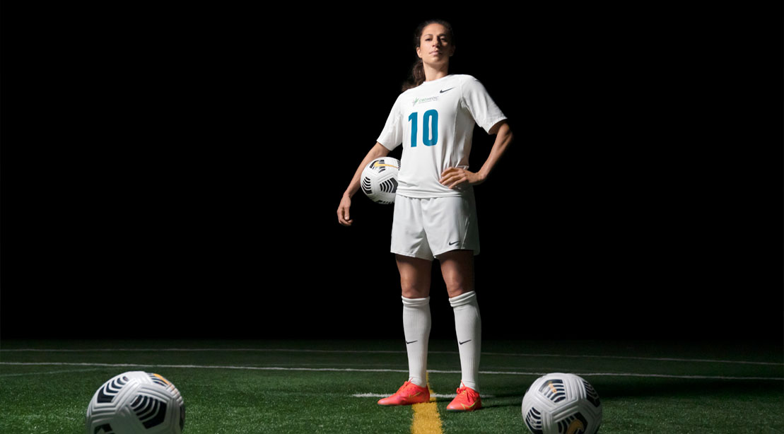 Carli Lloyd holding a soccer ball and standing on a soccer field