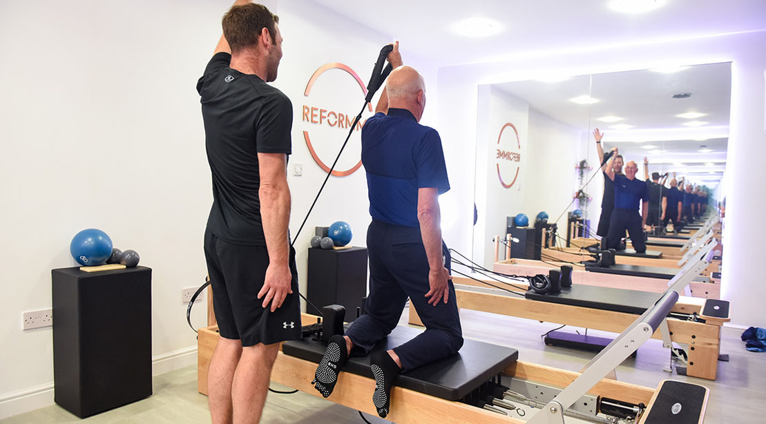 Old man training in pilates with a reformer pilates trainer