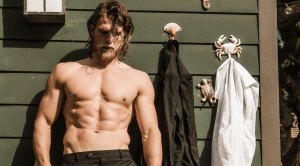 Travis Van Winkle leaning against a house with his shirt off showing his ab muscles