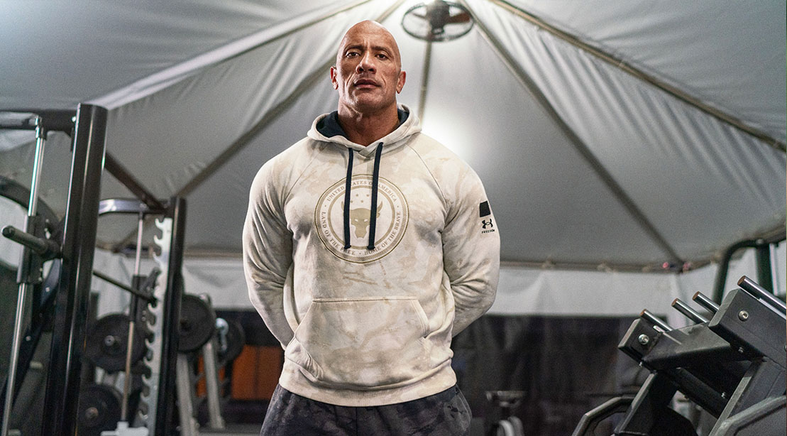 Dwayne Johnson aka The Rock wearing a project rock under armour white hoodie standing in the iron paradise