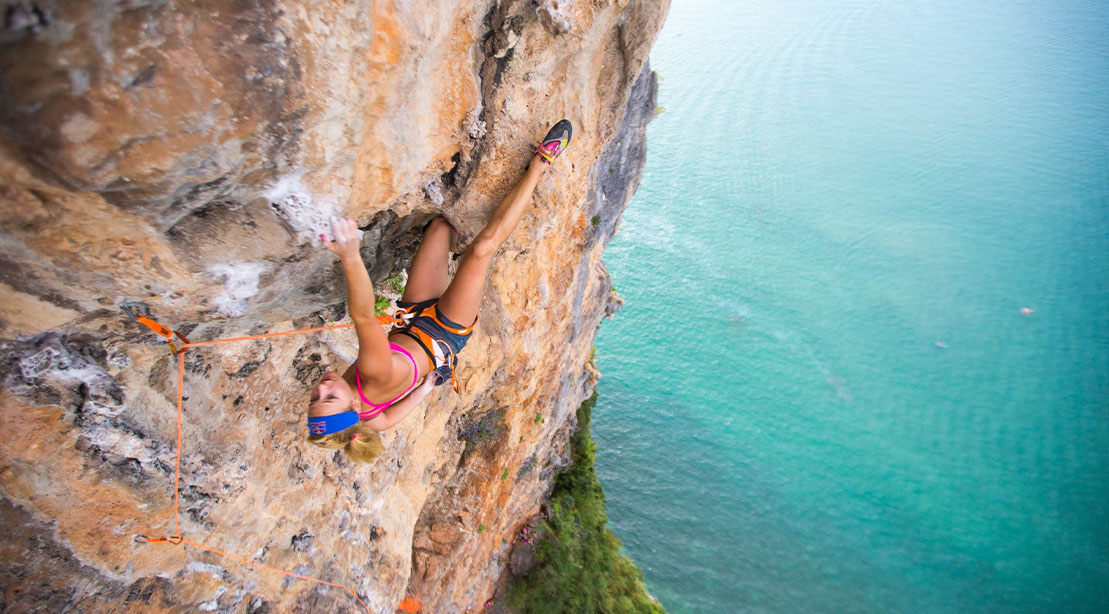 Female Rock Climber Sasha DiGiulian scaling the side of a cliff in a tropical climate